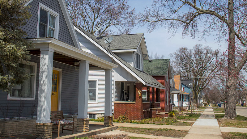 Row of Cape Cod style homes and a sidewalk with a blue home and a yellow door in front