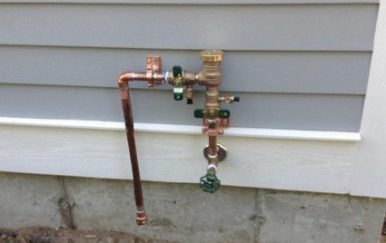 Copper pipe backflow prevention system on grey home
