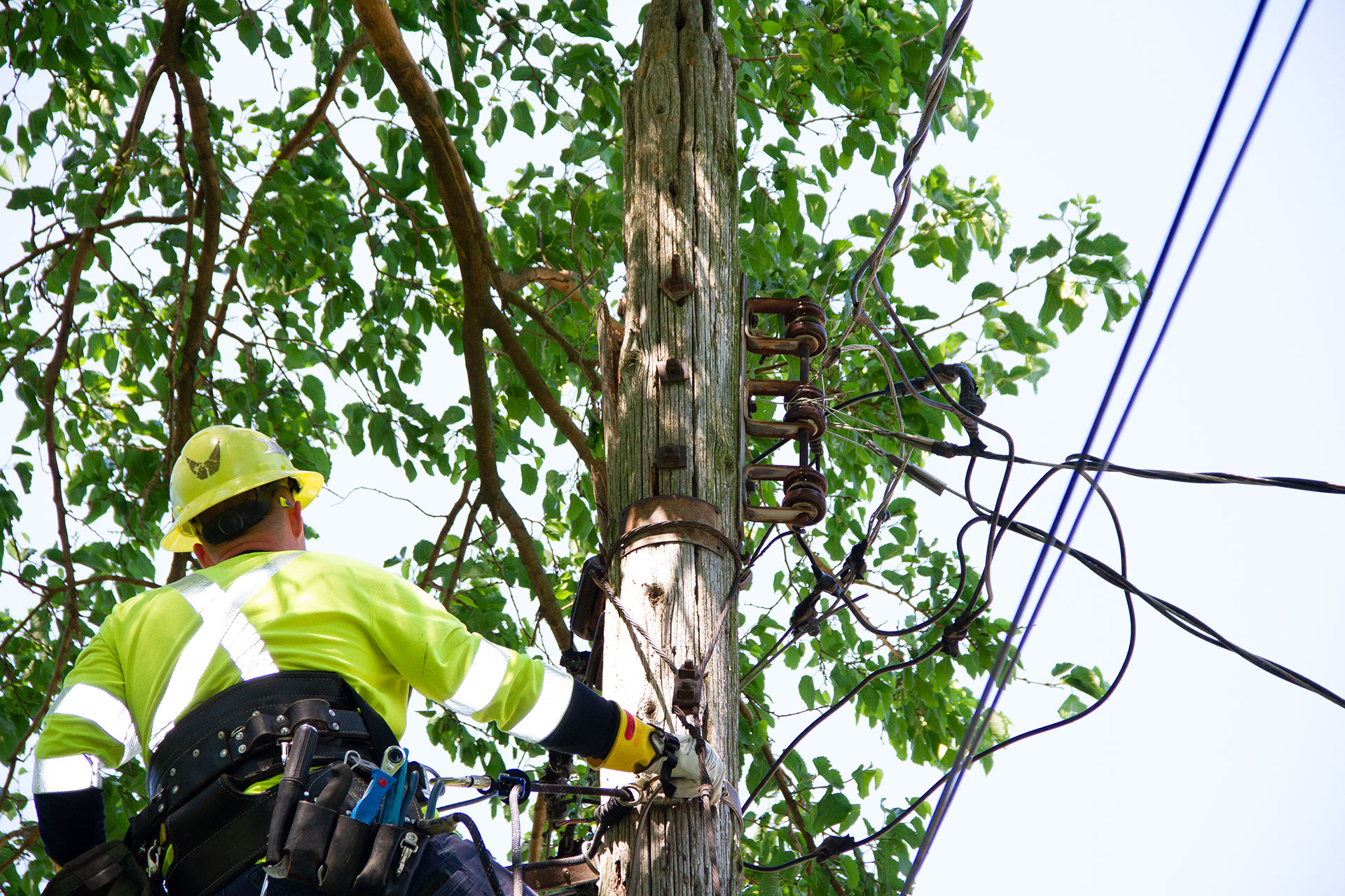 Lineman in high-vis clothing and a hard hat climbs a utility pole.