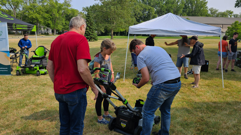 Adults crowded around an EGO lawnmower outdoors, setting in the battery.