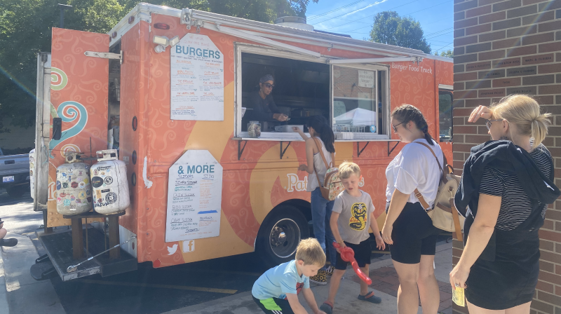 An orange food truck serves women and children in the sun