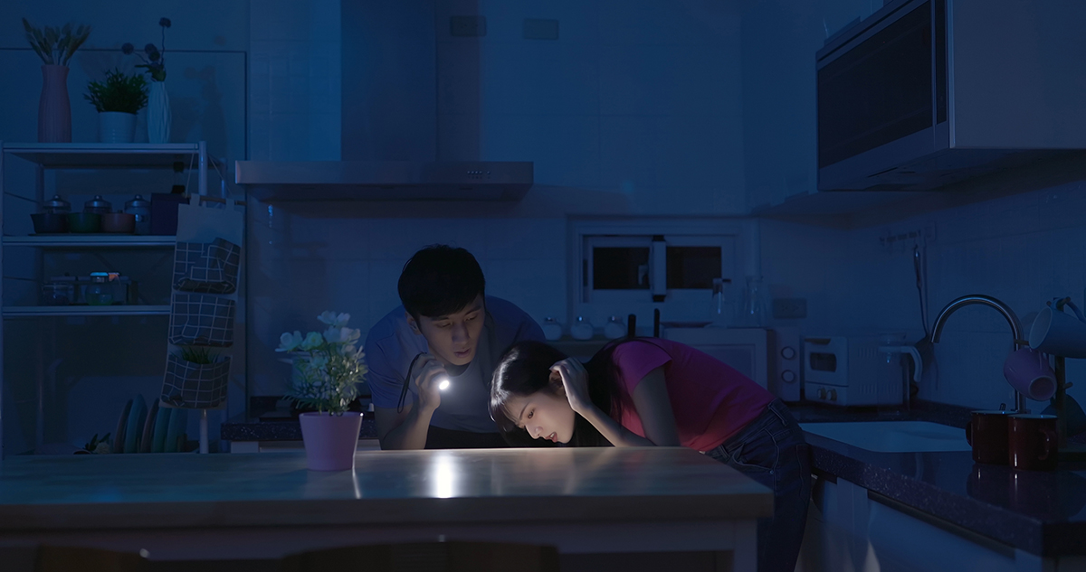 A couple uses a flashlight to look around the kitchen in the dark.