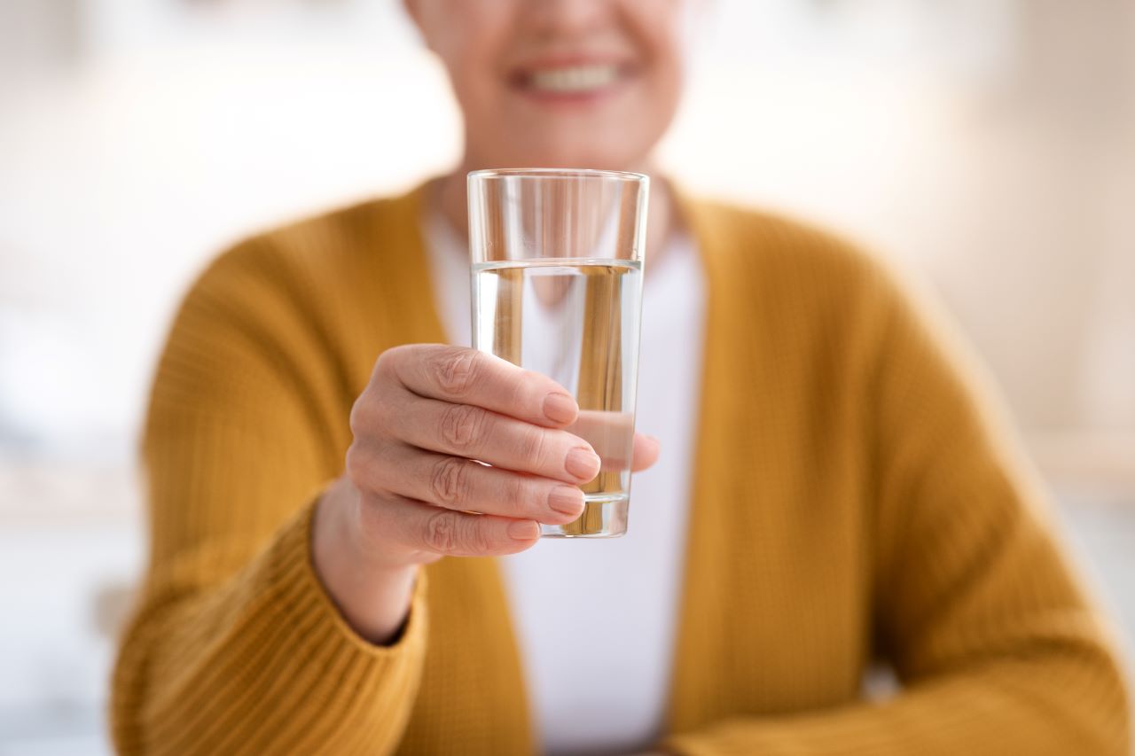 Woman in a yellow cardigan holds out water glass and smiles