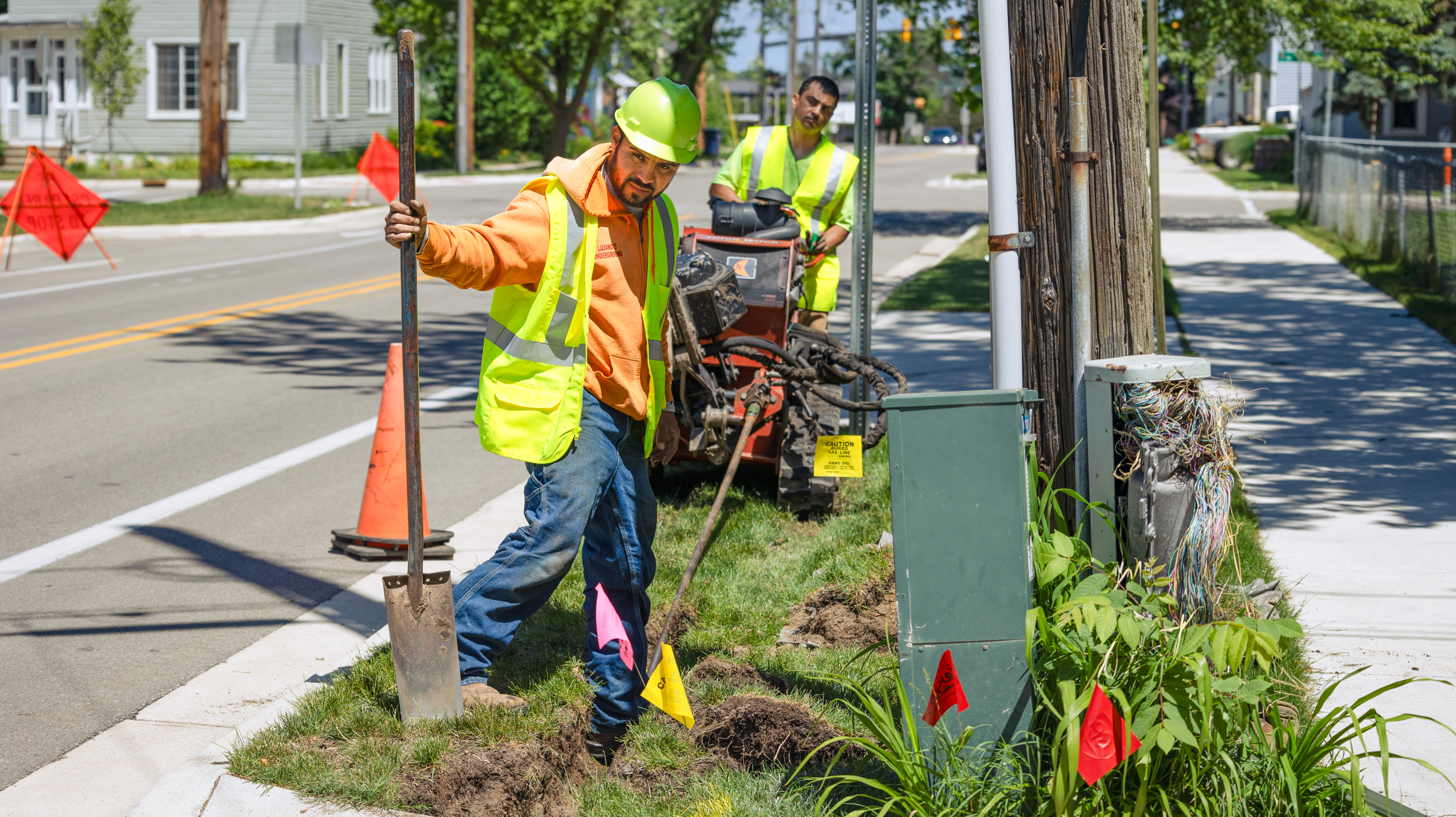 two fiber techs wearing reflective vests operate a boring rig