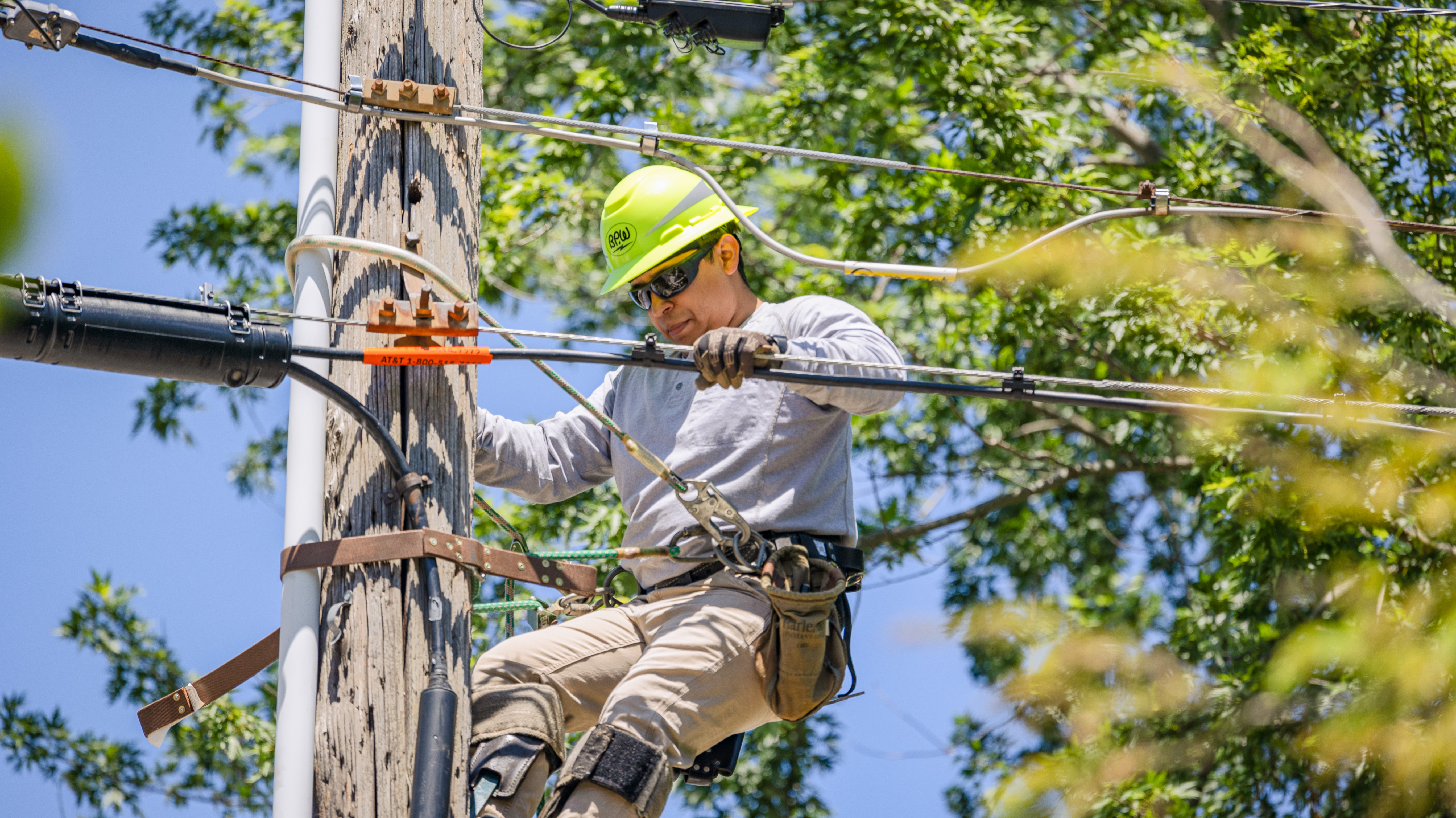 a man on utilility pole wearing a yellow hardhat