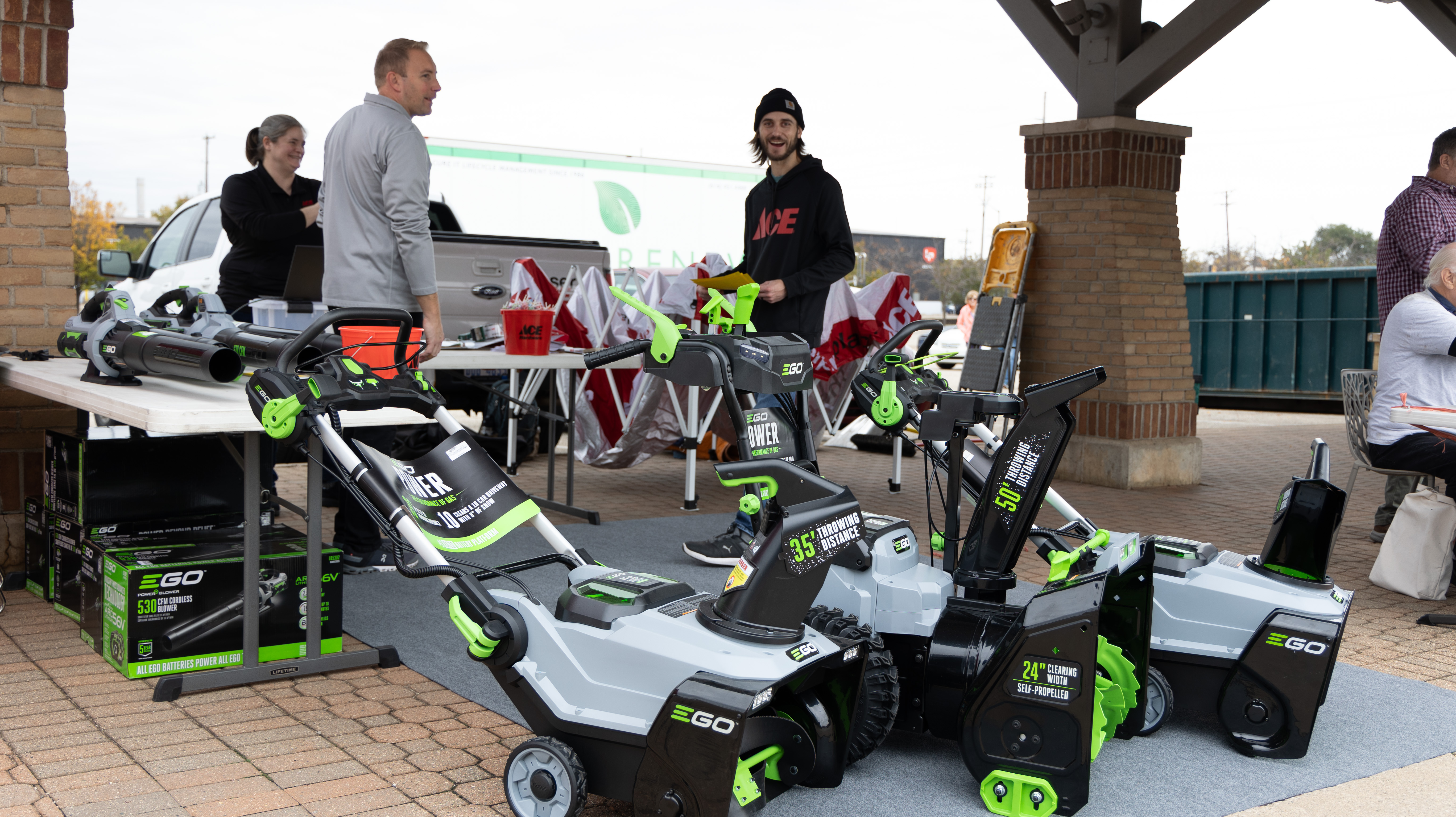 Visser Ace employees stand behind EGO snowblowers under an awning