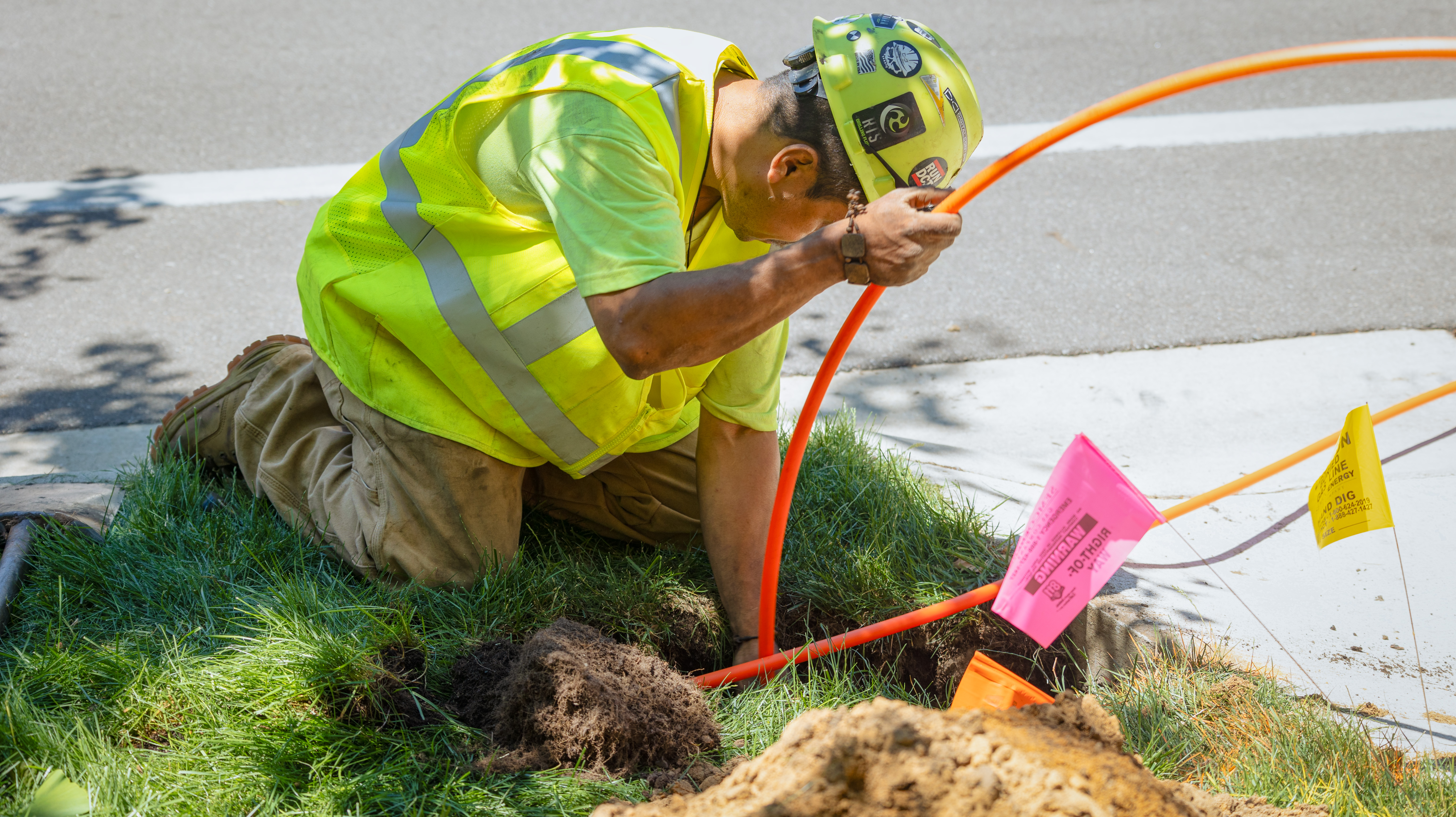 a fiber tech worker pulls oragne conduit through the ground