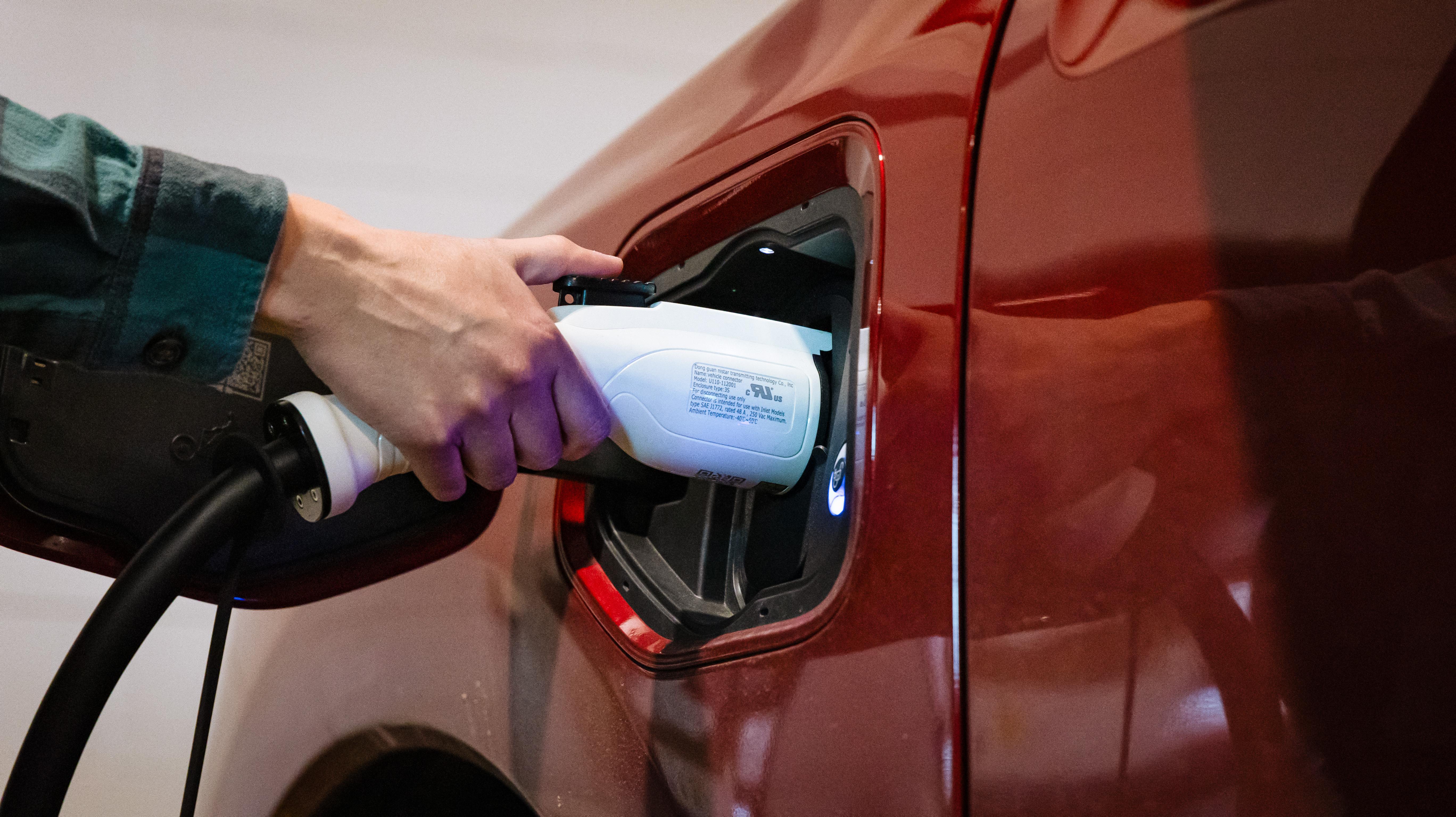 A hand plugs in an EV charger on a red vehicle.