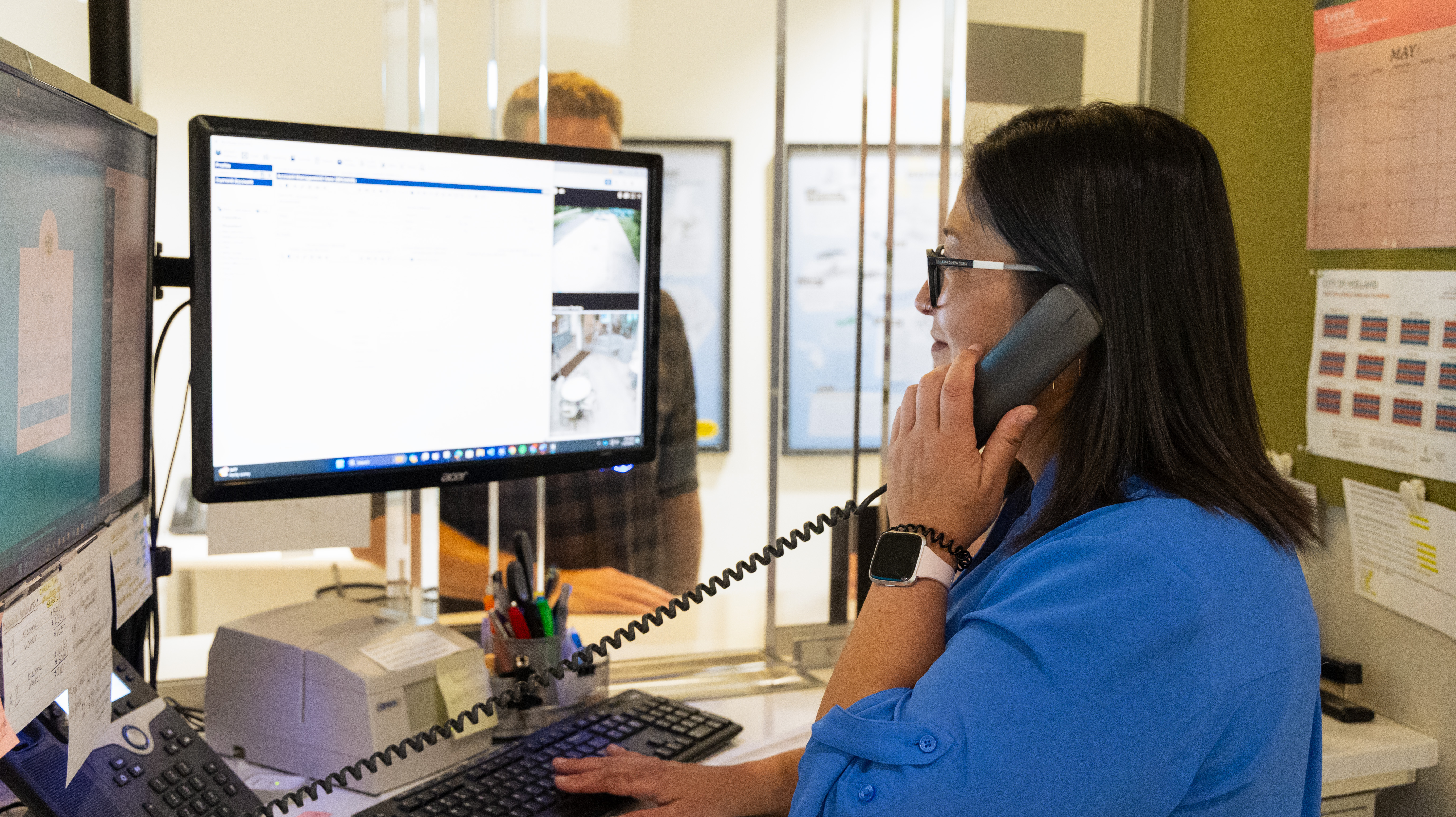 A woman in front of a computer while on the phone.