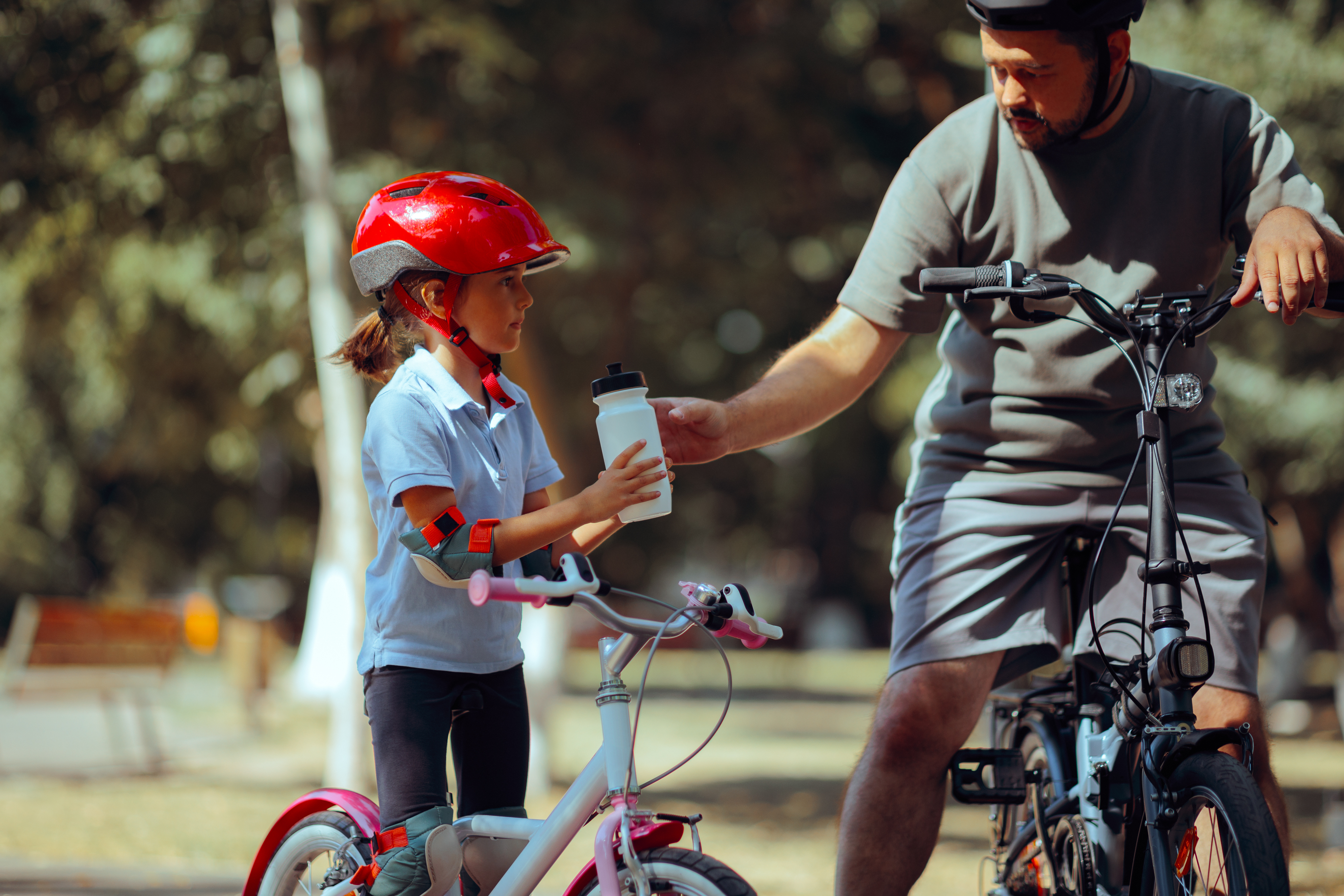 Father and daughter biking and stopping for a sip of water.
