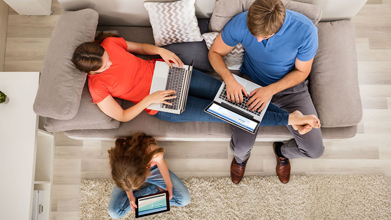 two adults and one child sitting together in a living room and using personal computers