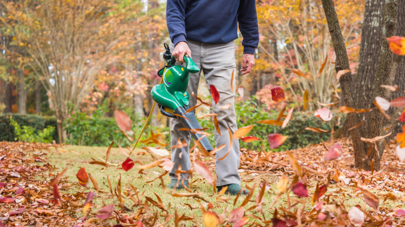 Man in khakis using a chorded electric leaf blower in a yard